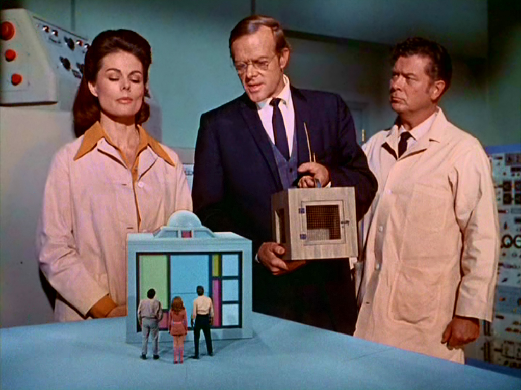 Three giants look down on three tiny humans on a tabletop