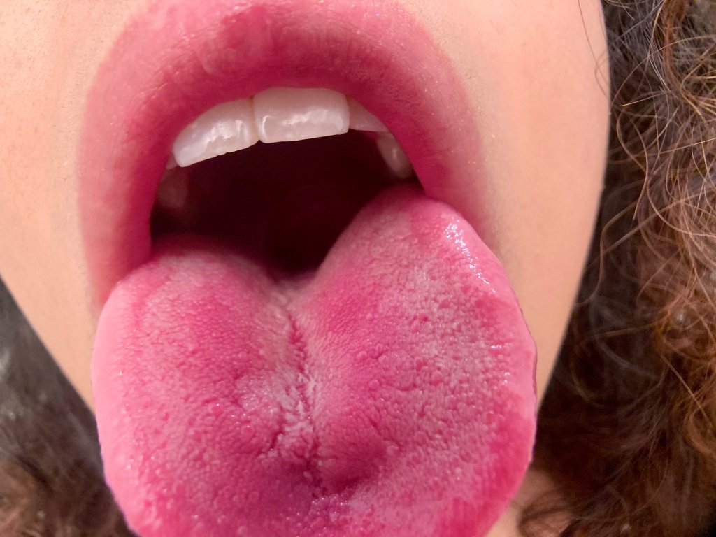 A close-up photo of a young woman's open mouth and extended tongue.